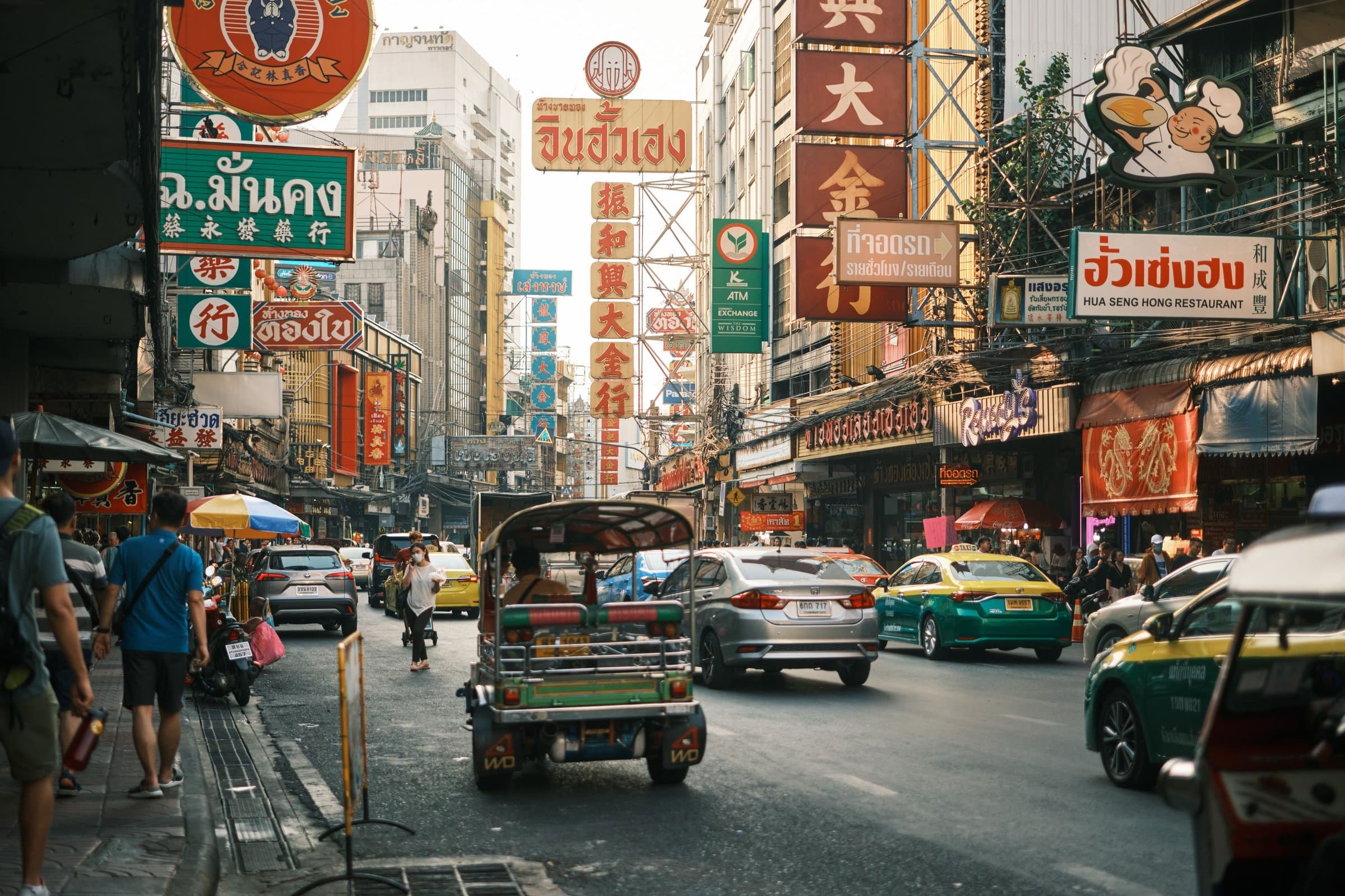 A tuk-tuk and taxis on a busy street lined with signs in Bangkok's Chinatown