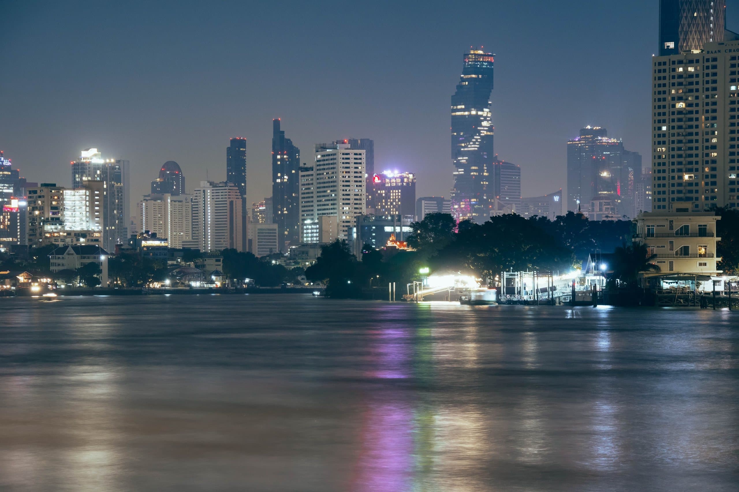 Bangkok's skyline at night across a river, with the Mahanakhon Tower